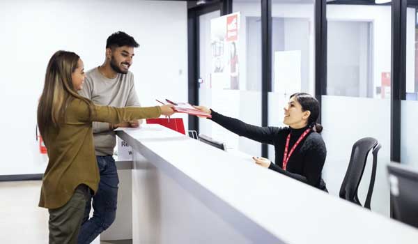 Two students engaging with a TAFE SA staff member, passing documents over a counter top.