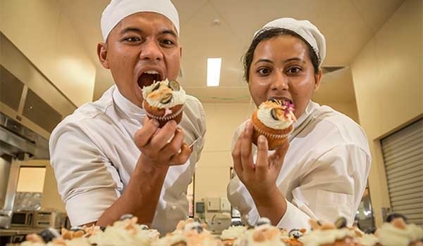 Two cookery students about to bite into Lemon and Blueberry muffins in hand